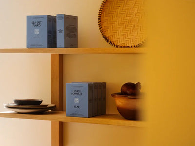 
                    
                      Havsnø Norwegian Sea Salt Flakes, light blue-gray boxes, multiple packs displayed on wooden shelves.
                    
                  