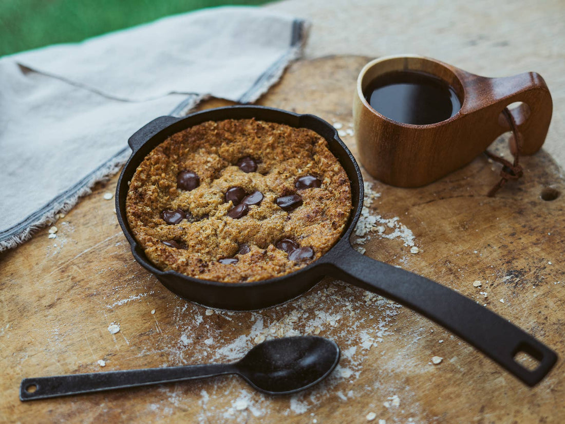 Cast Iron Skillet baking a chocolate chip cookie, served on a rustic wooden table with a black cast iron spoon.