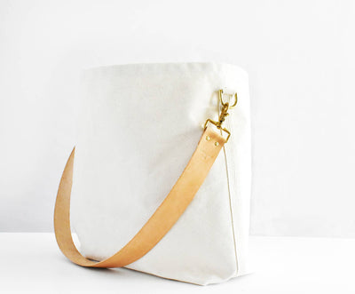 
                    
                      Celina Mancurti Everyday Tote Bag, natural cotton canvas with tan leather strap and brass hardware, standing upright front…
                    
                  