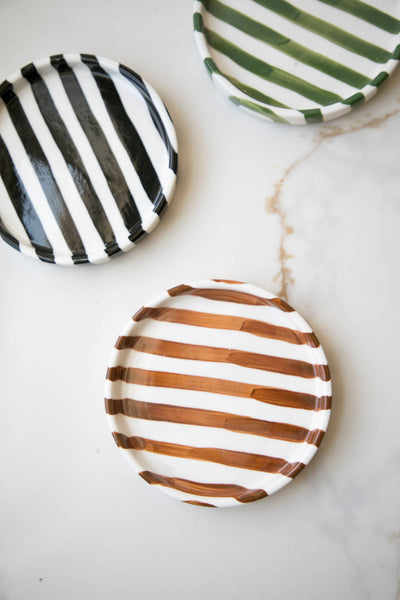 
                    
                      Striped ceramic plates, black, brown, and green with white stripes, overhead group view of three.
                    
                  