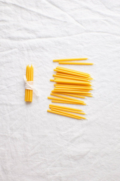 
                    
                      Waxing Moon Beeswax Birthday Candles, pure yellow beeswax. Flat lay of one bundle with white ribbon and many loose candles.
                    
                  