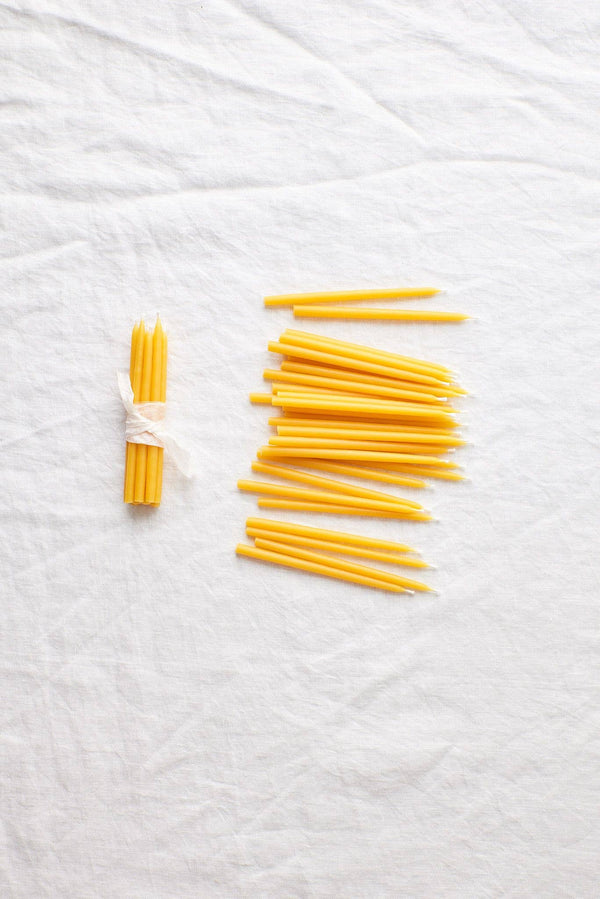 Waxing Moon Beeswax Birthday Candles, pure yellow beeswax. Flat lay of one bundle with white ribbon and many loose candles.