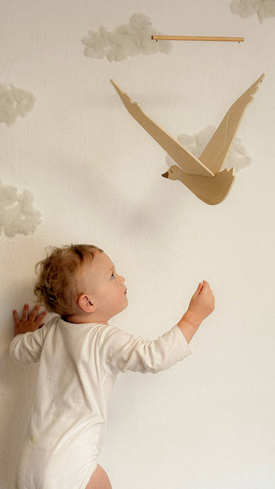 
                    
                      Wooden Flying Goose mobile, natural wood with cotton cord, seen with a child reaching up for scale.
                    
                  