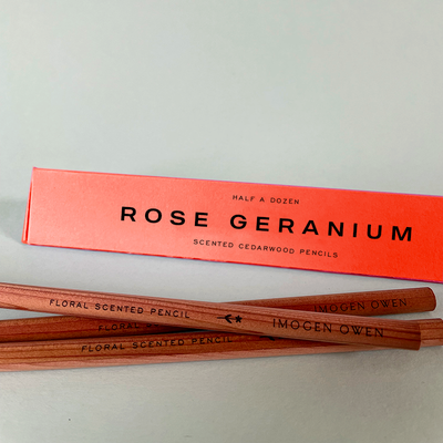 
                    
                      Imogen Owen Rose Geranium Scented Pencils, natural cedarwood pencils with coral box, flat lay close-up.
                    
                  