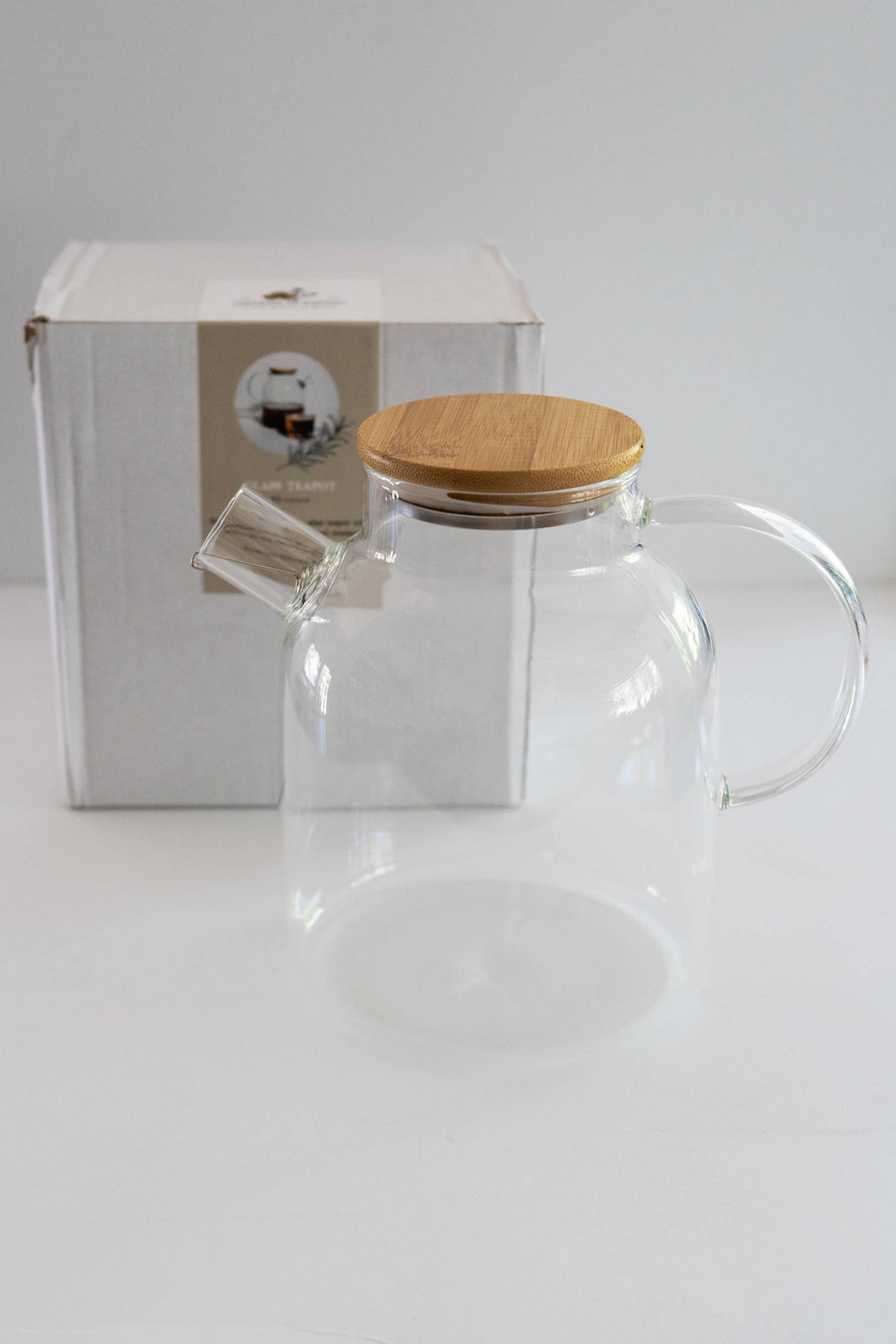60 Oz. Heat-Resistant Glass Teapot with bamboo lid, stainless steel infuser visible in spout. Packaging box in background.