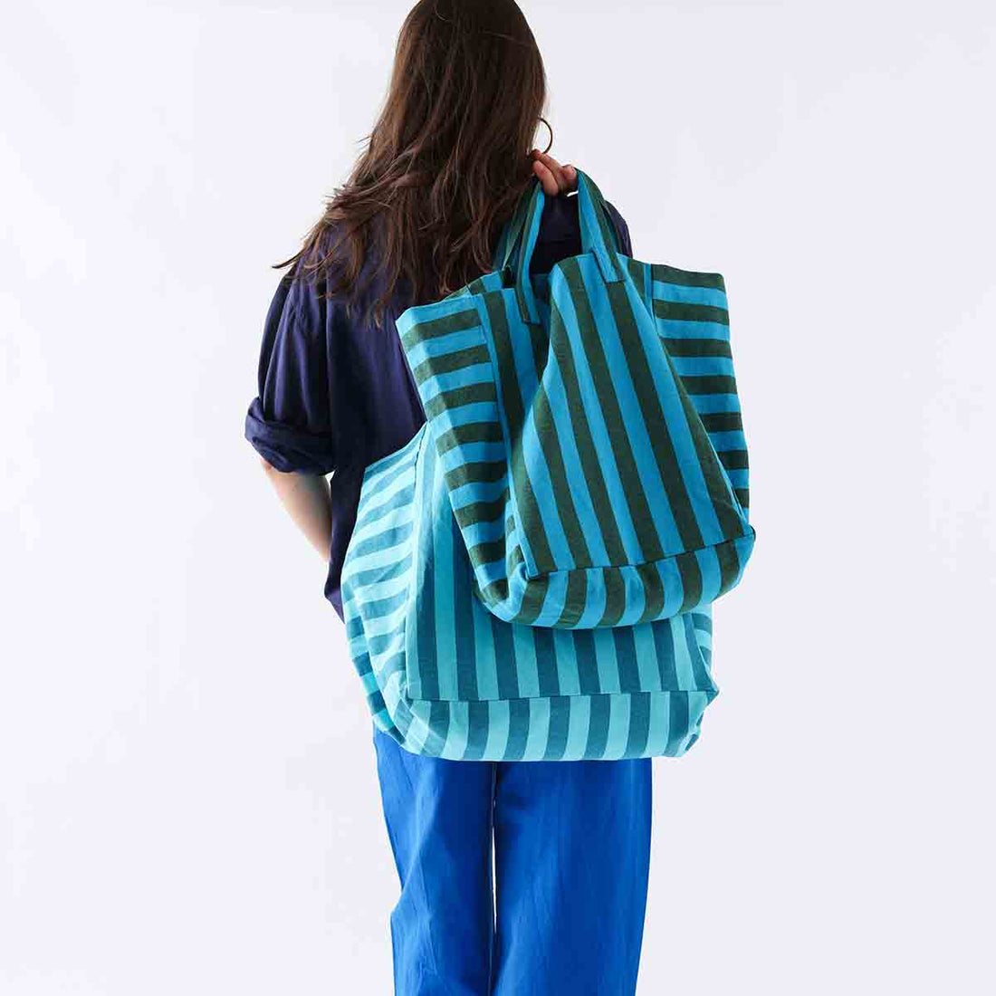 Elisabeth cotton tote bag in turquoise and olive stripes, carried over shoulder by person, back view, with a second matching…