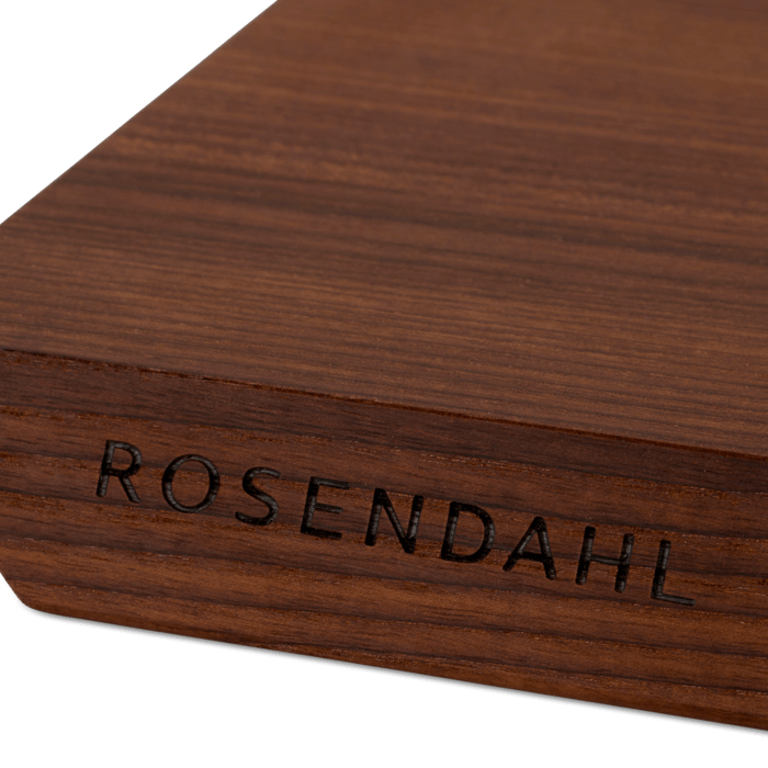 Rå wood cutting board, heat-treated ash, close-up of engraved ROSENDAHL logo and dark wood grain on the corner.