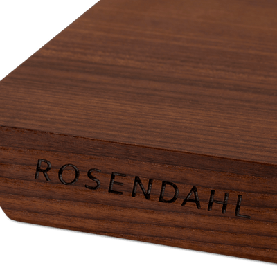 
                    
                      Rå wood cutting board, heat-treated ash, close-up of engraved ROSENDAHL logo and dark wood grain on the corner.
                    
                  