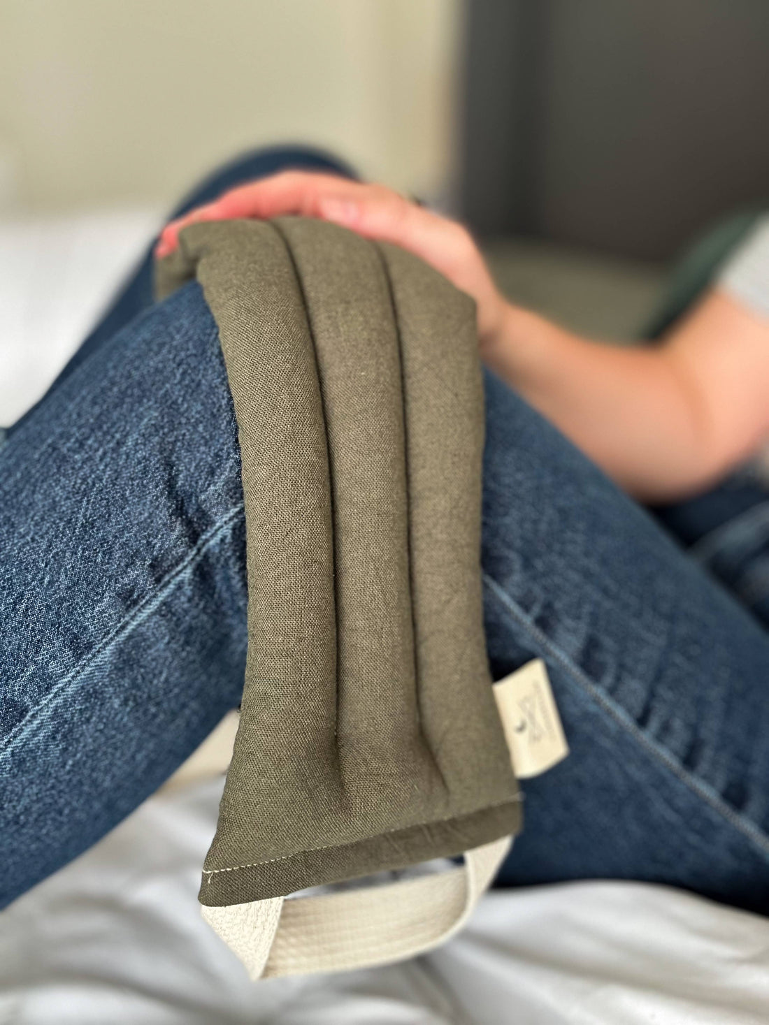 Olive Microwaveable Neck Wrap, cotton and linen blend canvas, resting on a person's leg, highlighting its flexible texture.