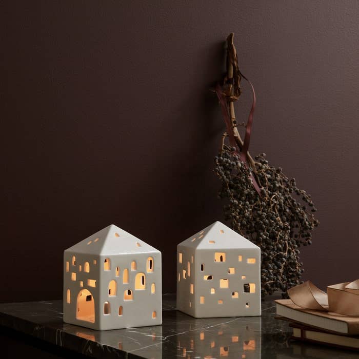 Two Urbania Lighthouse ceramic candle holders, one Town House style, glowing white on a dark marble surface.