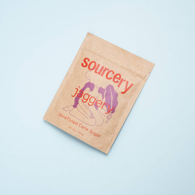 
                    
                      Sourcery Jaggery sweetener, unrefined cane sugar in kraft paper pouch with red and purple branding, angled flat lay.
                    
                  