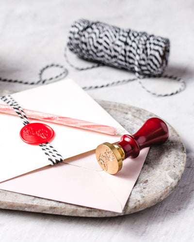 
                    
                      Wax Seal Stamp Set with red handle and brass snowflake head, sealing a pink envelope with red wax.
                    
                  