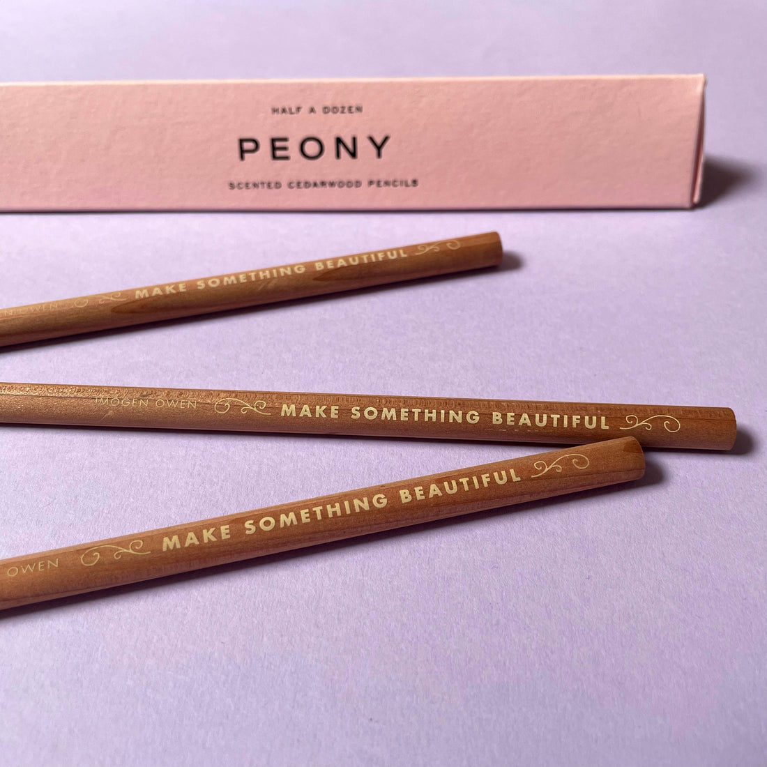 Imogen Owen Peony Scented Pencils, three cedarwood writing pencils with gold foil lettering, angled in front of pink box.