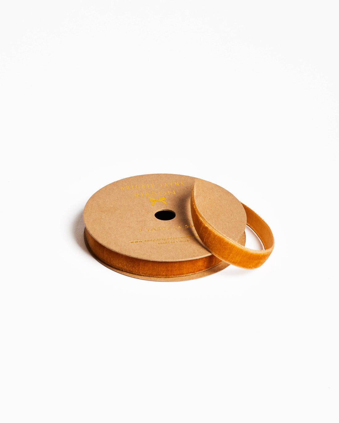 Amber velvet ribbon on kraft paper spool, partially unwound, showing product label, angled view.