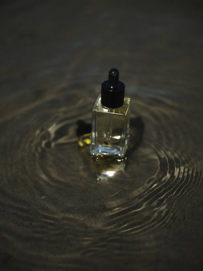 
                    
                      Shave Oil in square clear glass bottle with light golden oil and black dropper, resting in dark rippling water.
                    
                  