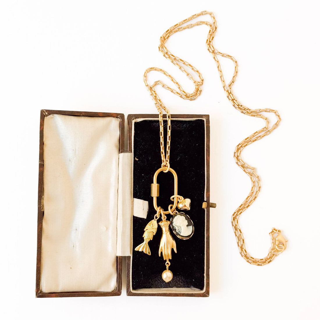 Gold Carabiner Charm Necklace with fish, hand, cameo, and pearl charms, displayed in open antique jewelry box.