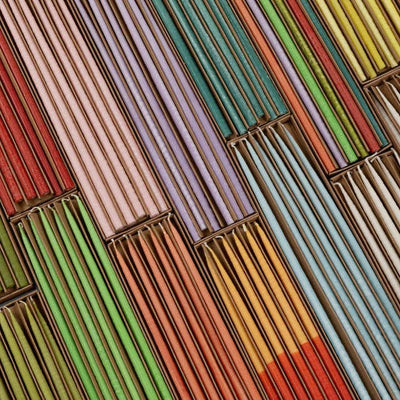 
                    
                      Thin Rainbow taper candles, vibrant multi-color wax, multiple sets in their brown paper packaging, diagonal overhead view.
                    
                  