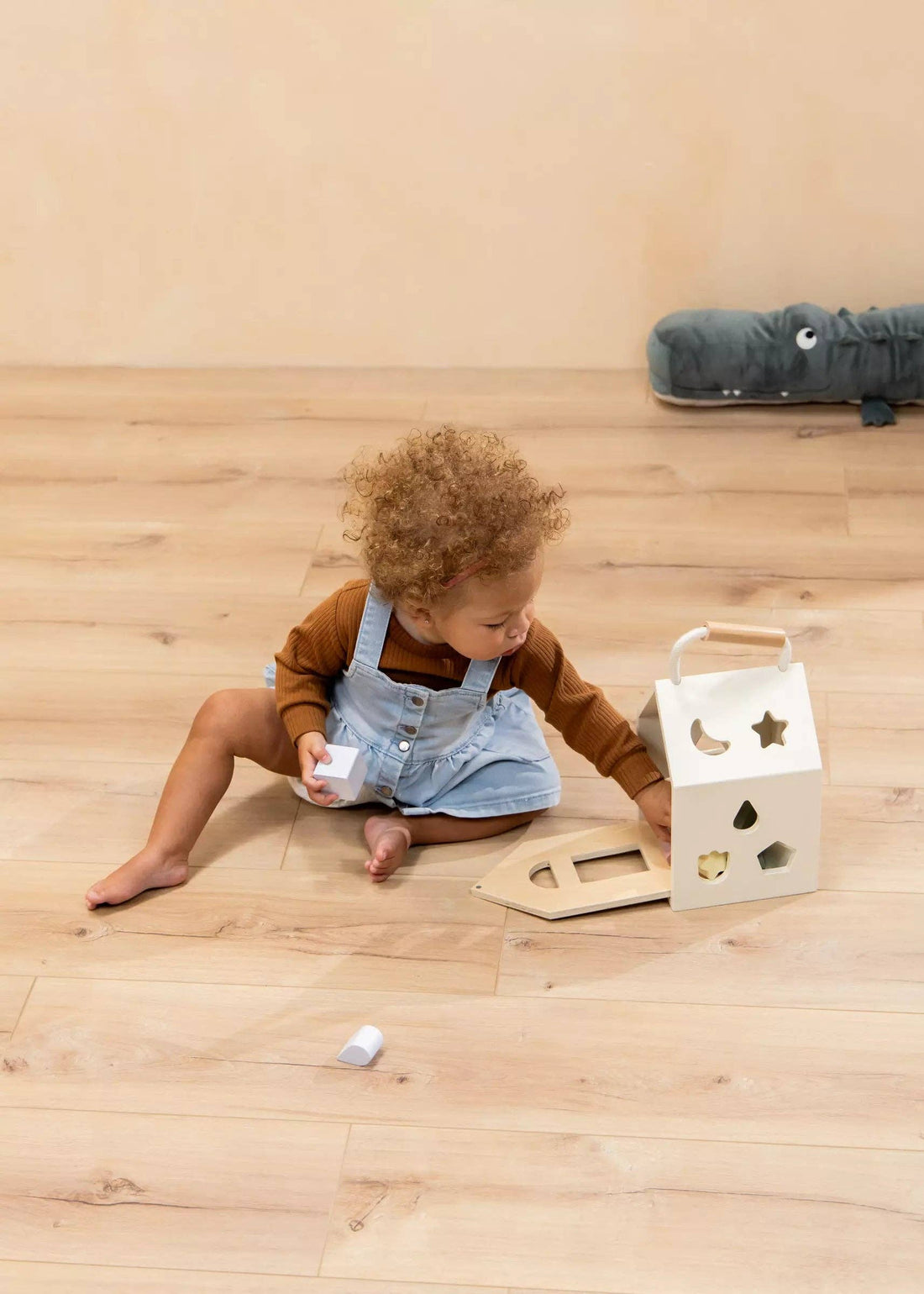 Wooden Shapes Sorting House, natural wood and white, baby playing on light floor, placing a white shape piece.