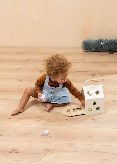 
                    
                      Wooden Shapes Sorting House, natural wood and white, baby playing on light floor, placing a white shape piece.
                    
                  