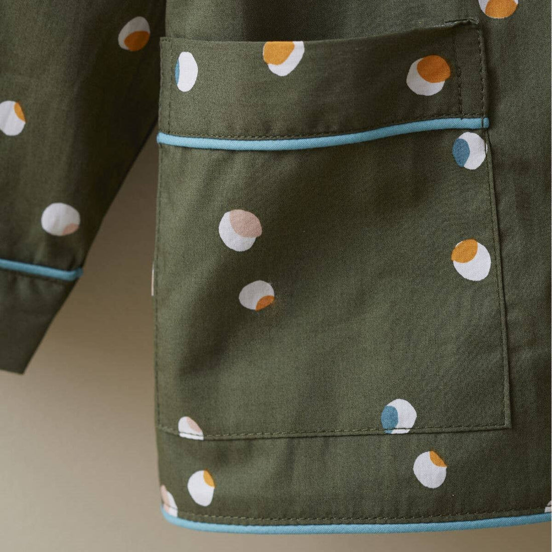 Kids Confetti Pajamas, olive green cotton with multi-color dots, close-up of front pocket and sleeve with light blue piping.