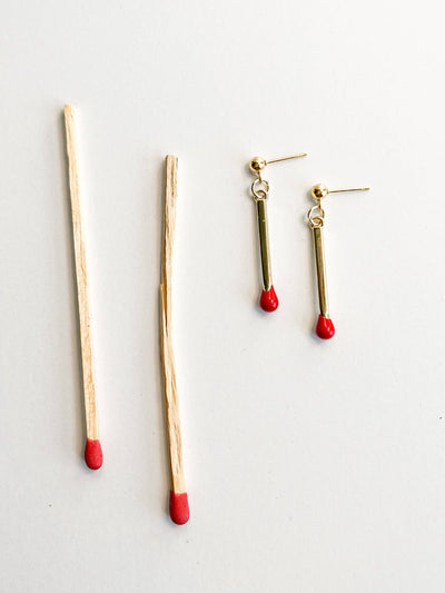 
                    
                      Matchstick drop earrings, 18k gold plated with red tips, flat lay next to real matchsticks for scale comparison.
                    
                  