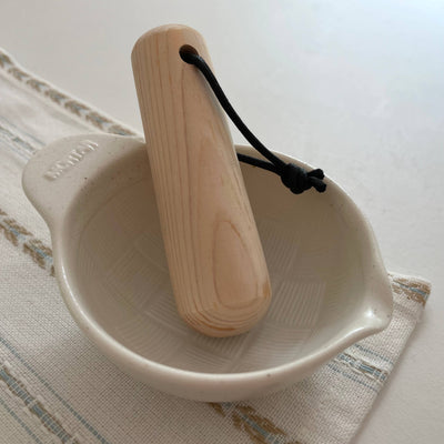 
                    
                      Japanese Ceramic Mortar, white porcelain with textured interior, natural wood pestle with black cord, angled top-down view.
                    
                  