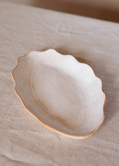 
                    
                      Handcrafted Stoneware Tray, speckled off-white with natural clay wavy edge, angled view on light fabric
                    
                  