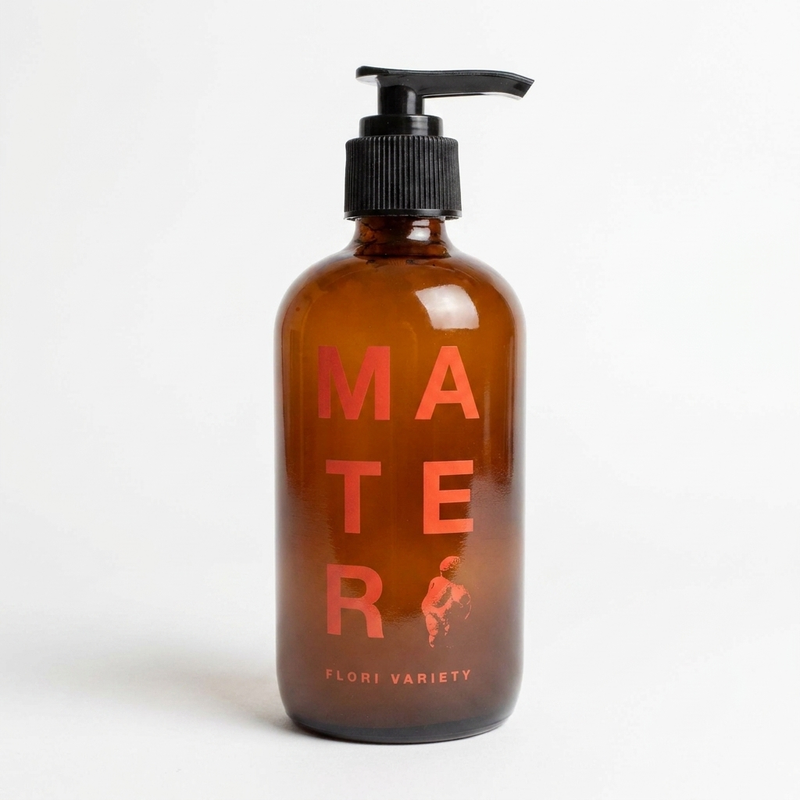Mater Soap Flori liquid hand soap in amber glass bottle with black pump and red lettering, front on white.
