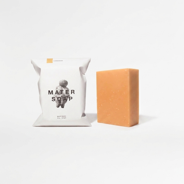 Mater Soap Geranium Soap Bar, light orange, displayed unwrapped beside its white branded package, front view.