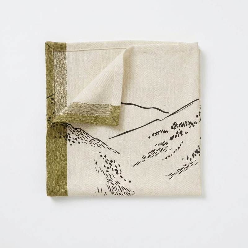 Sylvie Thiriez Grandeur Nature Napkin, cream textile with black mountain landscape pattern and olive green border, folded…