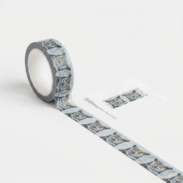 Blackbird Letterpress Great Horned Owl washi tape, grey repeating owl head pattern with yellow eyes, roll unspooling.