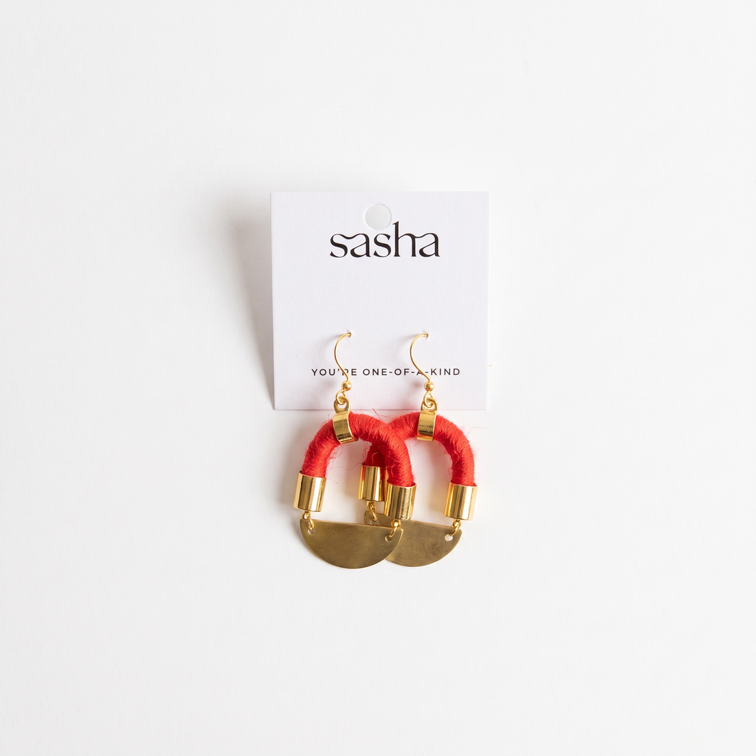 Sasha Half Moon earrings, red yarn-wrapped cording with brass moon pendants and gold-plated hardware, flat lay on product…