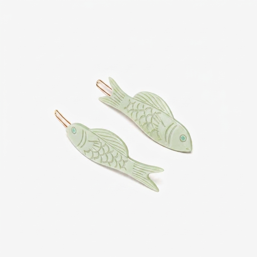 Winona Irene Jade Fish Barrette Set, green acetate with engraved scales, gold-toned clips, angled flat lay on white.