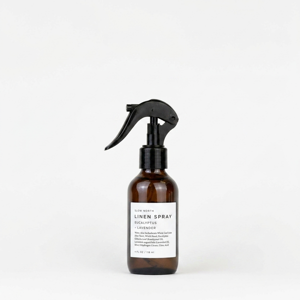 Slow North Linen Spray, Eucalyptus + Lavender, brown glass bottle with black spray nozzle, white label, front view on white.