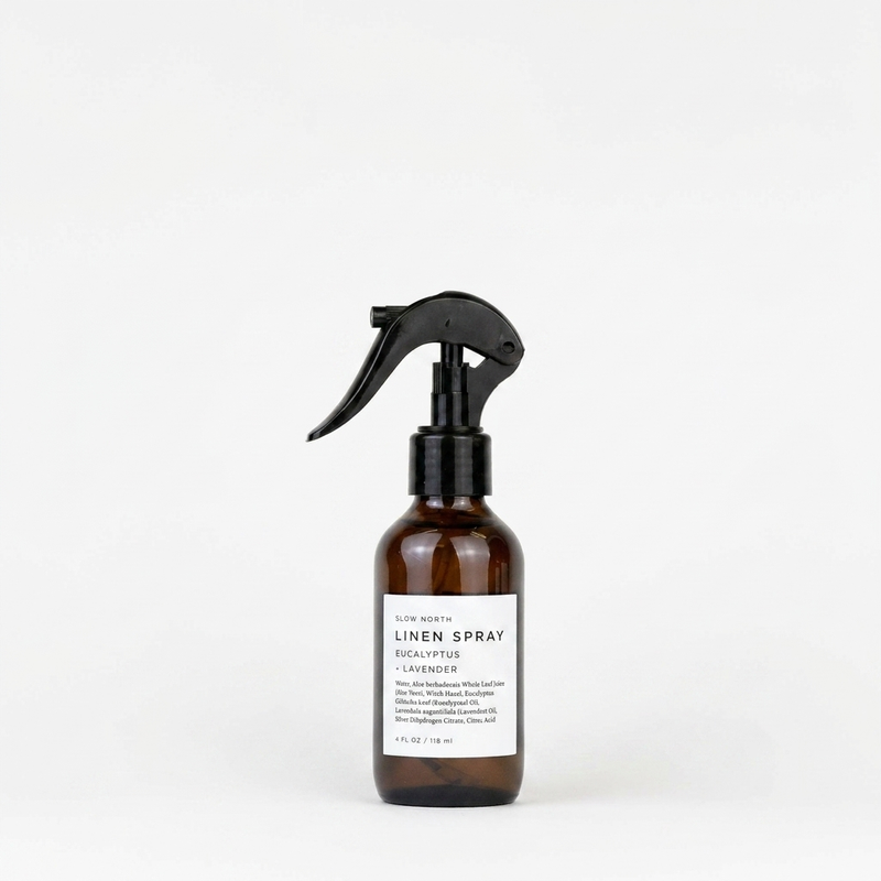 Slow North Linen Spray, Eucalyptus + Lavender, brown glass bottle with black spray nozzle, white label, front view on white.