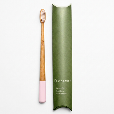 
                    
                      Truthbrush Petal Pink bamboo toothbrush, natural wood handle with pink tip, standing upright next to its olive green package.
                    
                  