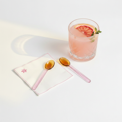 
                    
                      Casa Amarosa Pink and Amber borosilicate glass stirring spoons, flat lay pair on white next to pink cocktail.
                    
                  