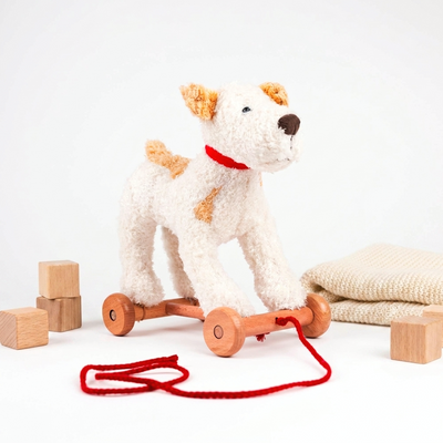 
                    
                      Egmont Plush Pull-Along Eliot Dog, white polyester plush with tan spots, red collar, natural wood wheels, 3/4 front view.
                    
                  