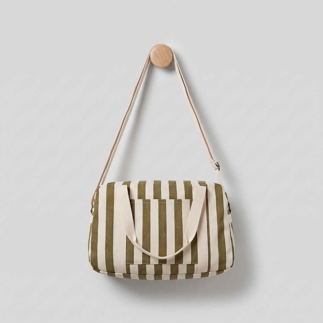 Rose in April Raphael Weekend / Diaper Bag - (Olive + Greige) studio product photo hanging from a wooden wall hook on a…