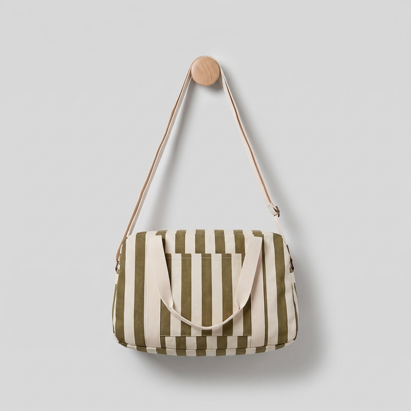 Rose in April Raphael Weekend / Diaper Bag - (Olive + Greige) studio product photo hanging from a wooden wall hook on a…