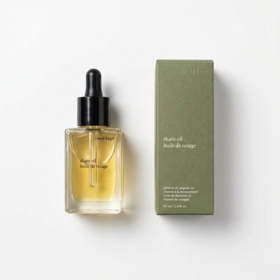 
                    
                      Well Kept Shave Oil, clear glass bottle with amber oil and black dropper, next to olive green product box, flat lay.
                    
                  
