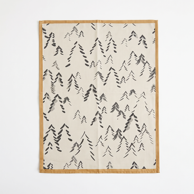 
                    
                      Spitzberg cotton tea towel, off-white with dark gray abstract trees, tan stitched border, flat lay.
                    
                  