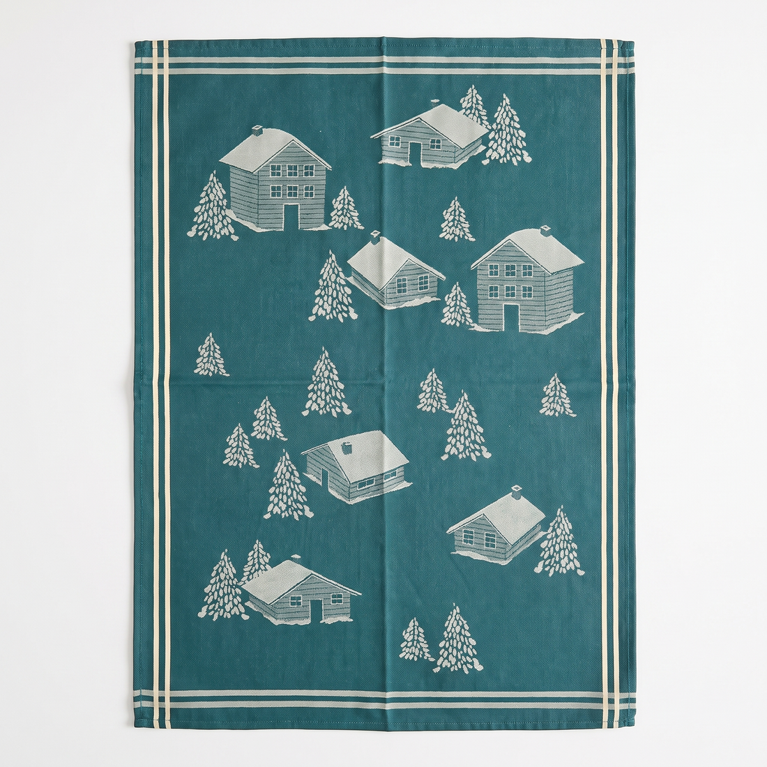 Coeur Vallée tea towel, blue 100% cotton jacquard with full pattern of white winter cabins and pine trees, flat lay.