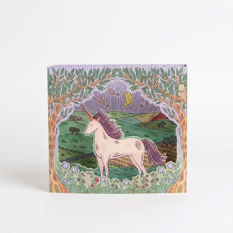 Art Angels Twilight Unicorn die-cut card, illustrated by Fee Greening, green landscape, purple trees, front on white.