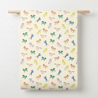 
                    
                      Red Cap Cards Wild Horses wrapping paper, multi-colored horse pattern on cream recycled paper, full roll view held by wooden…
                    
                  