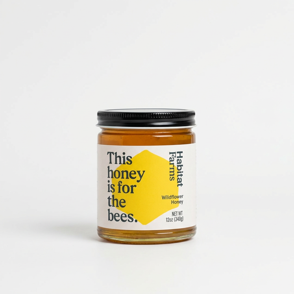 Habitat Farms Wildflower Honey jar, amber honey in clear glass with black lid and cream label featuring yellow hexagon,…
